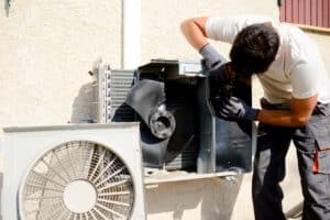 young man electrician installer working on outdoor compressor unit air conditioner at client's home